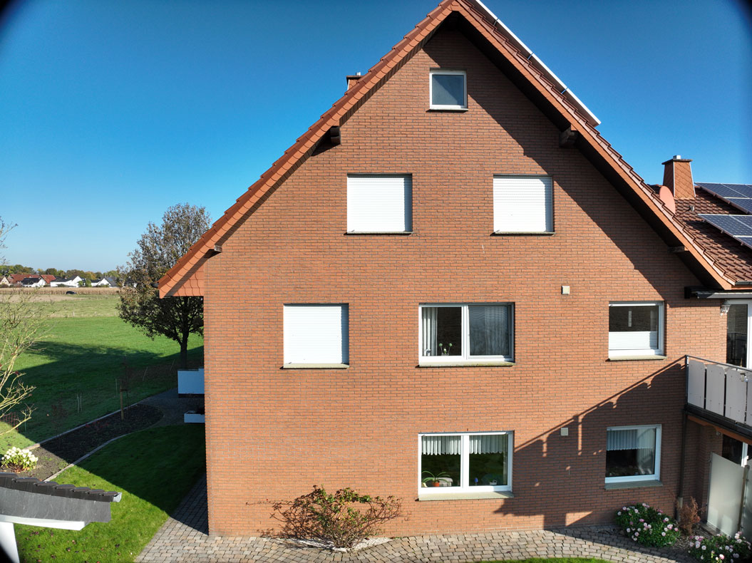 Ein rotes Backsteinhaus mit Dachziegeln, umgeben von einem grünen Garten und einem klaren blauen Himmel.